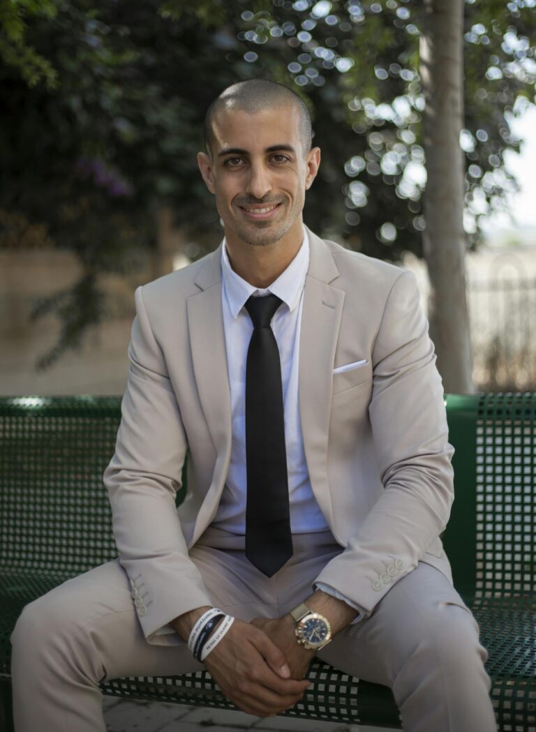 Professional businessman in a beige suit sitting on a bench outdoors, exuding confidence.